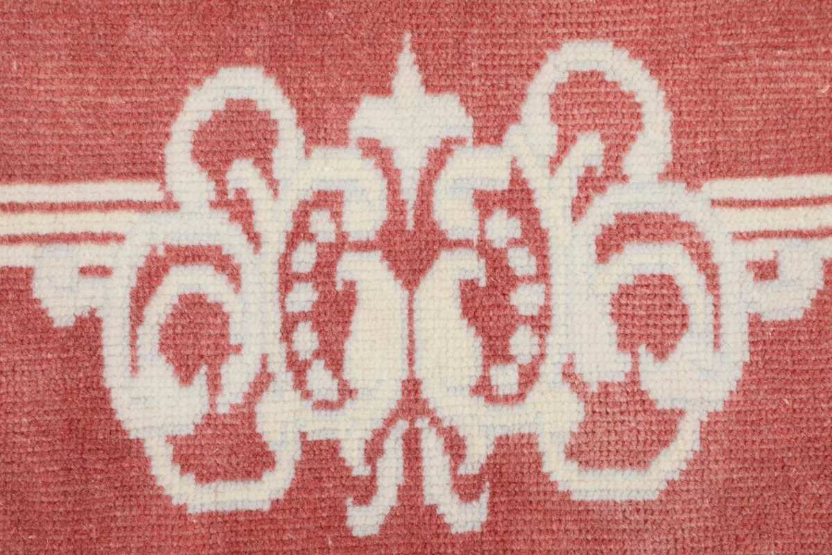 Close-up of a decorative scroll motif in ivory against the rose background