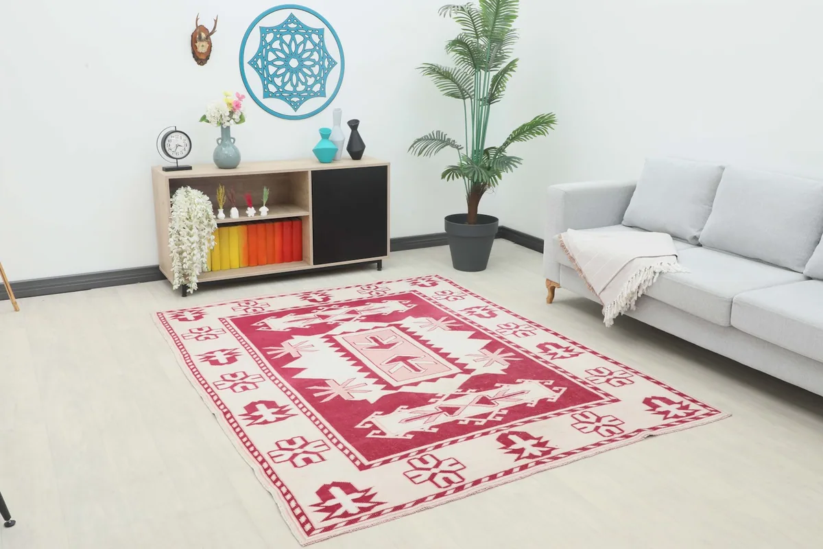Vintage red and ivory tribal rug displayed in a modern living room setting with a gray sofa and wooden cabinet.