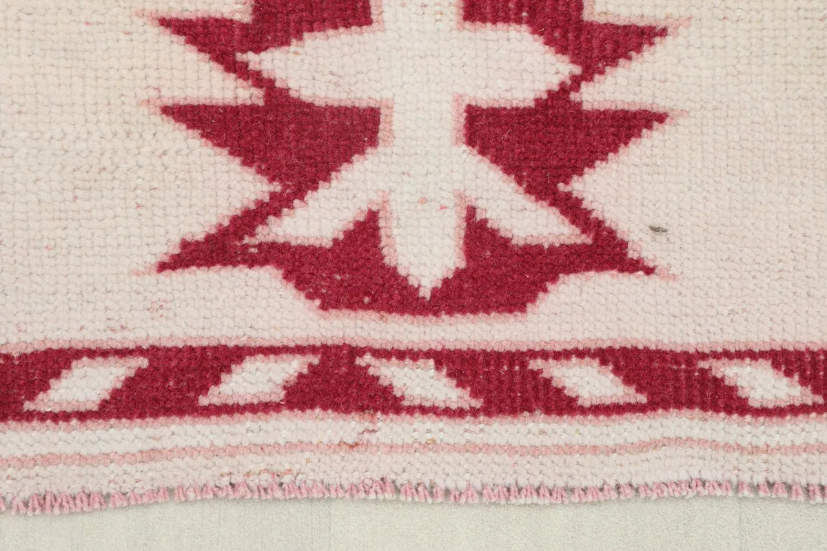 Close-up view of the rug's border showing red geometric motifs on an ivory background and low pile texture.
