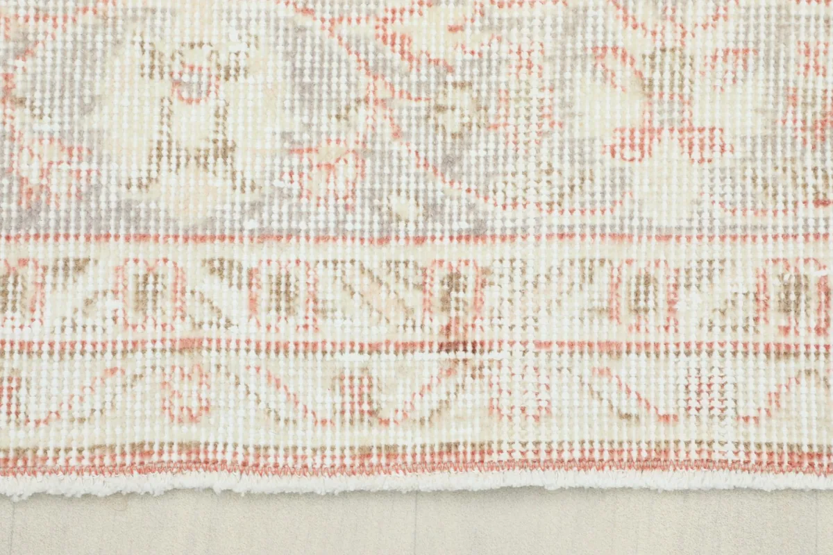 Close-up detail of the rug's short fringe and border pattern in rose, ivory, and gray tones.