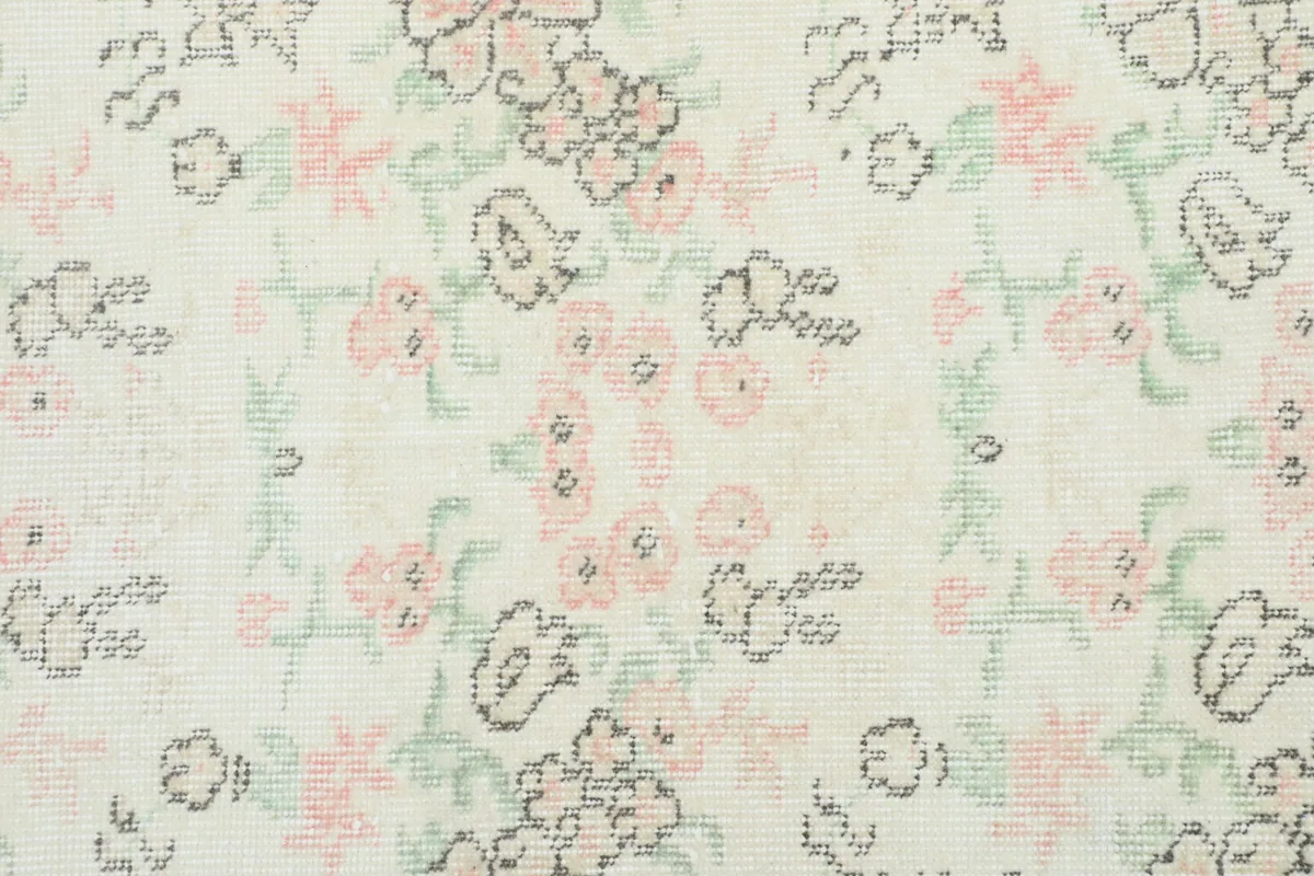 Detailed view of the hand-knotted floral motifs in pink, green, and gray on the cream field
