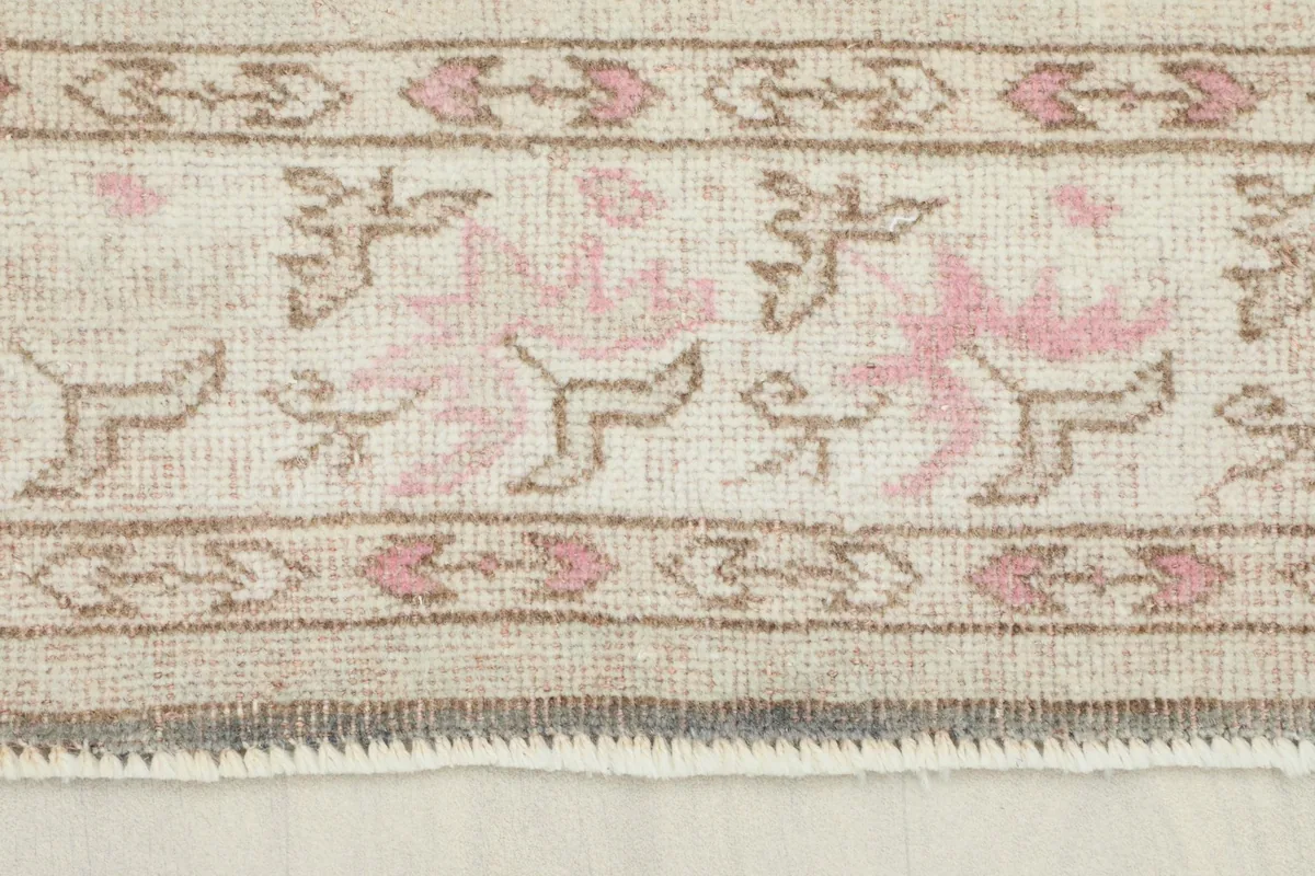 Close-up detail of the pink and beige tribal motifs in the rug's border.