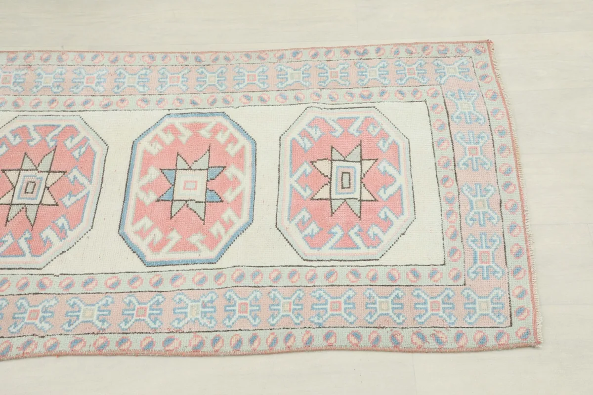 Close-up view of the runner's geometric medallions in rose and blue with the ivory field.