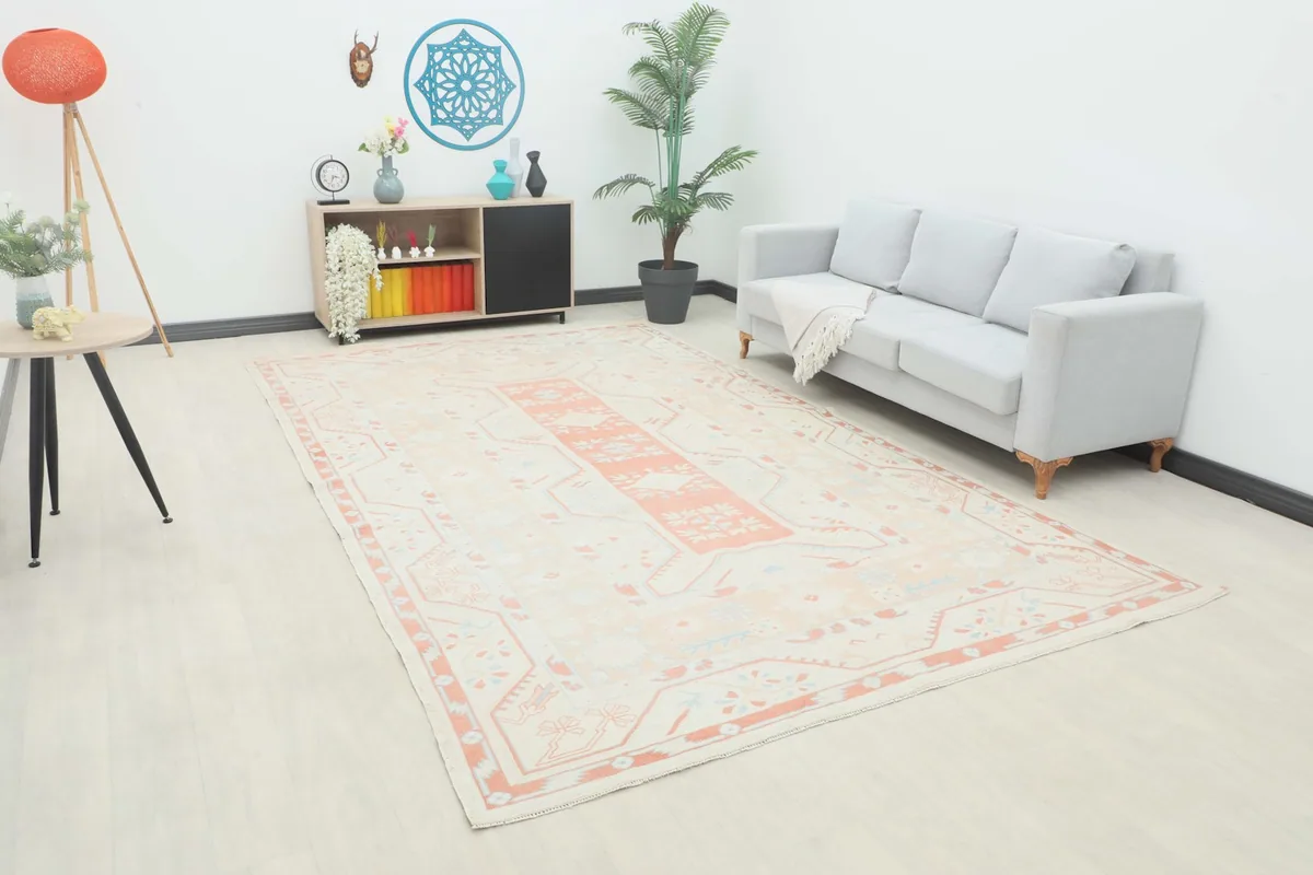 Large cream and rose vintage rug displayed in a modern living room setting with a gray sofa
