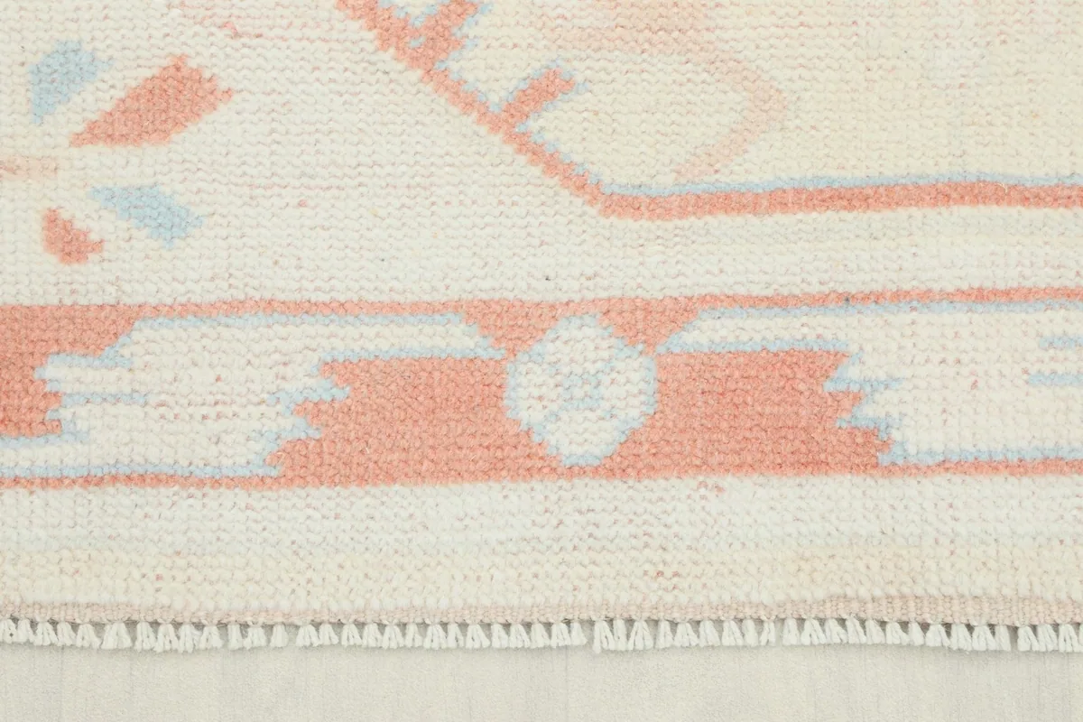 Close-up view of the rug's border and short fringe, showing the cream and rose colors