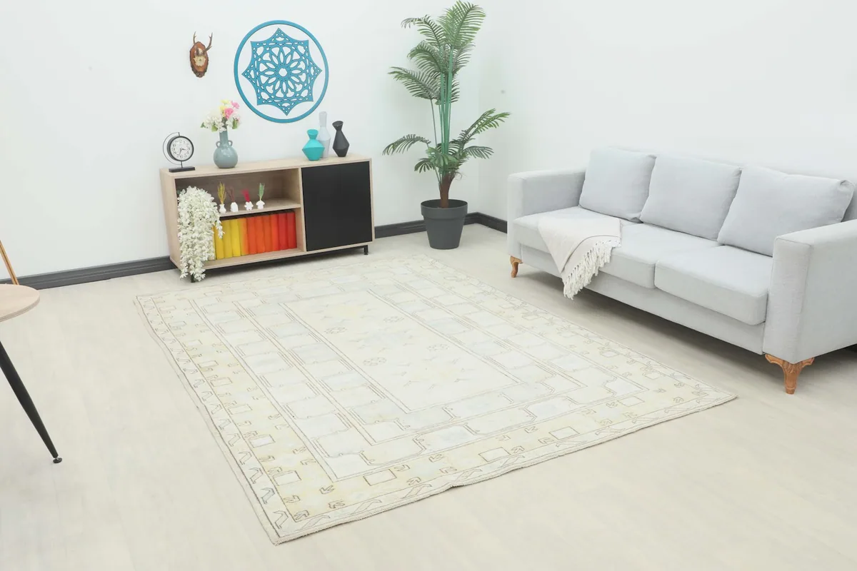 Ivory and beige Anatolian rug displayed in a living room setting with a gray sofa and light wood furniture.