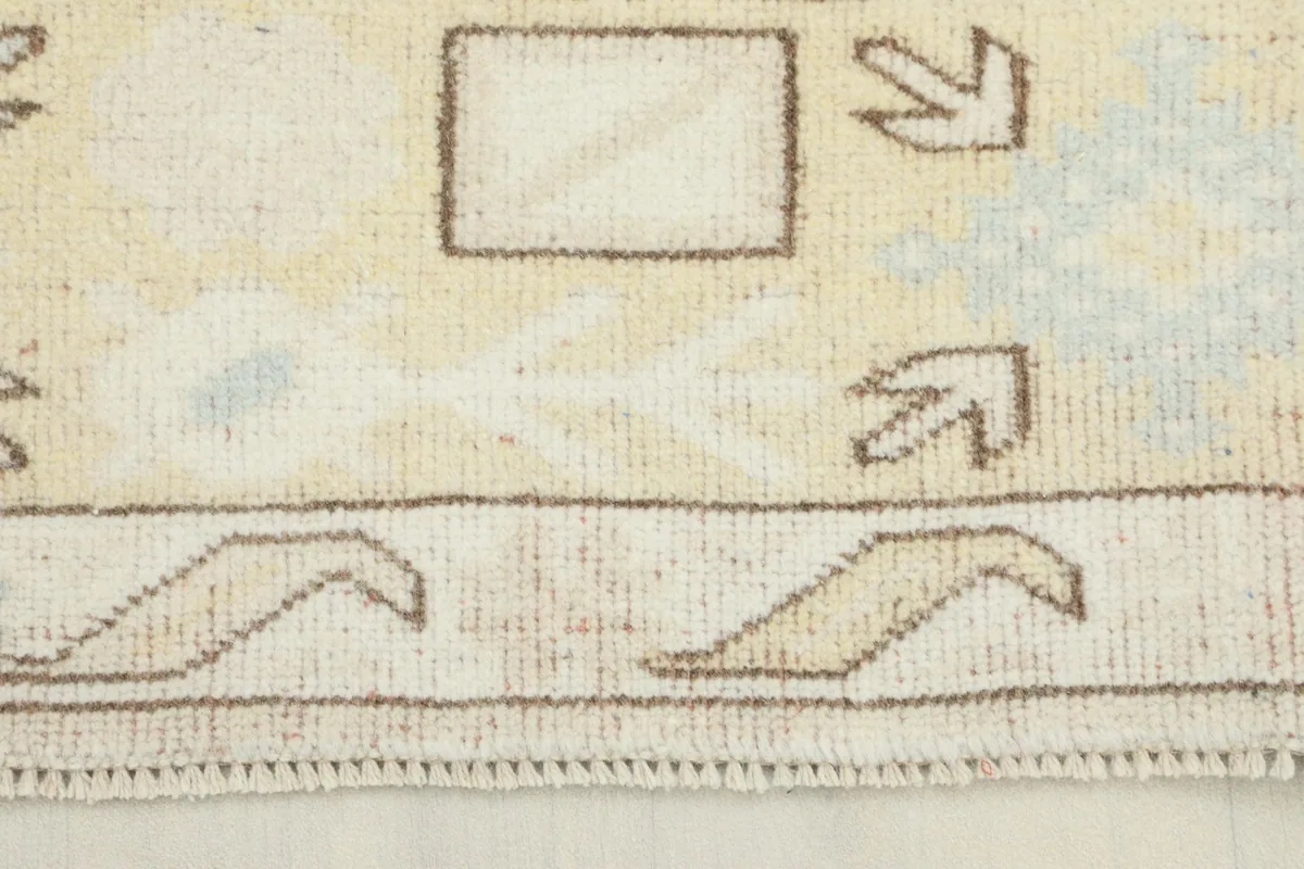 Close-up view of the rug's edge, showing the tan geometric border and subtle blue accents.