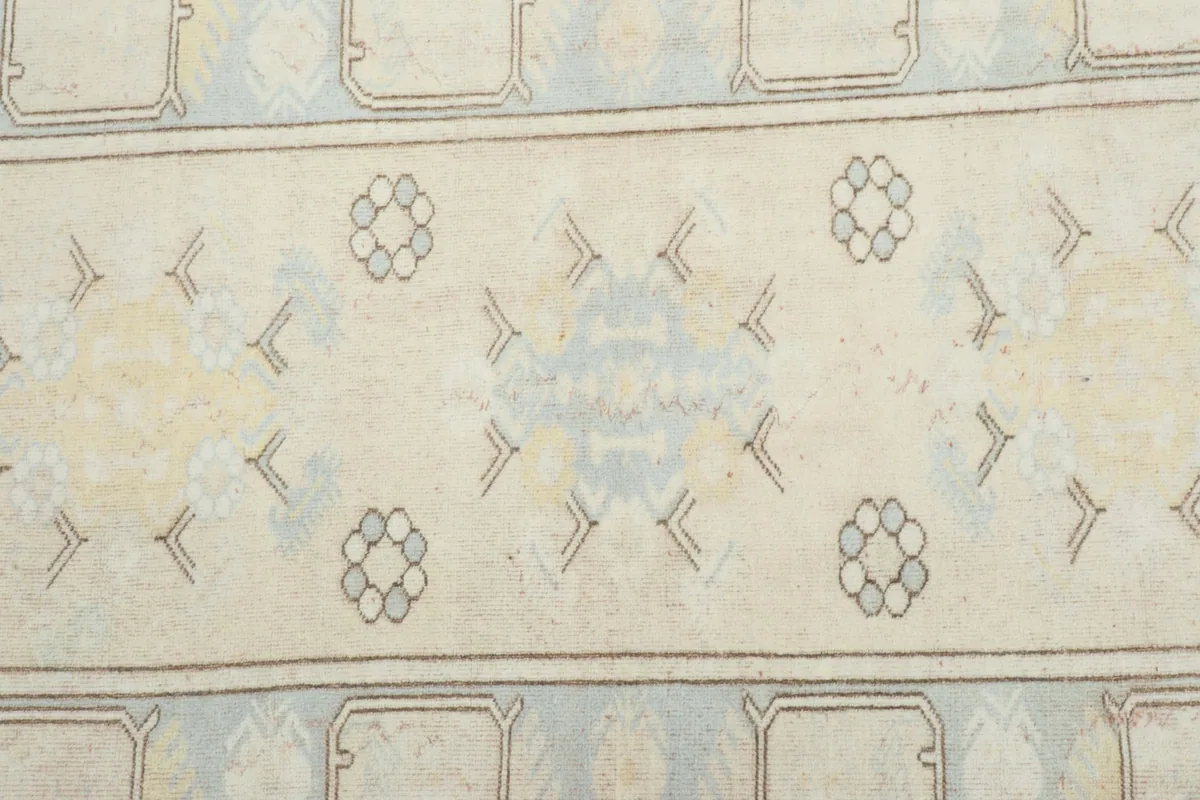 Detailed view of the rug's central field with geometric motifs and soft blue and beige tones.