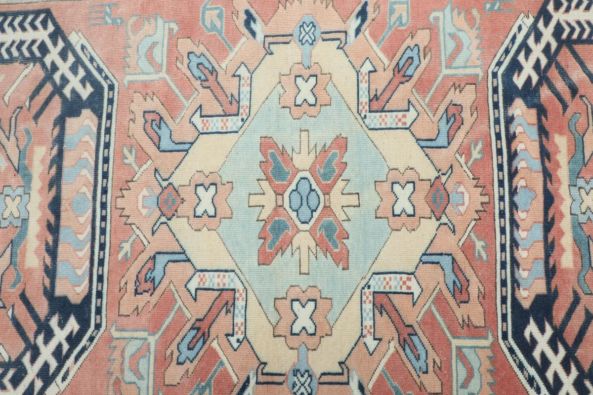 Detailed view of the rug's central medallion and surrounding geometric motifs in rose, ivory, and blue tones.