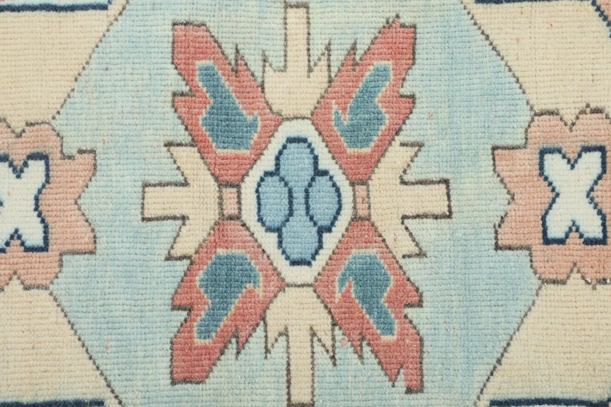 Zoomed-in shot of the intricate blue, rose, and ivory pattern within the central medallion of the rug.