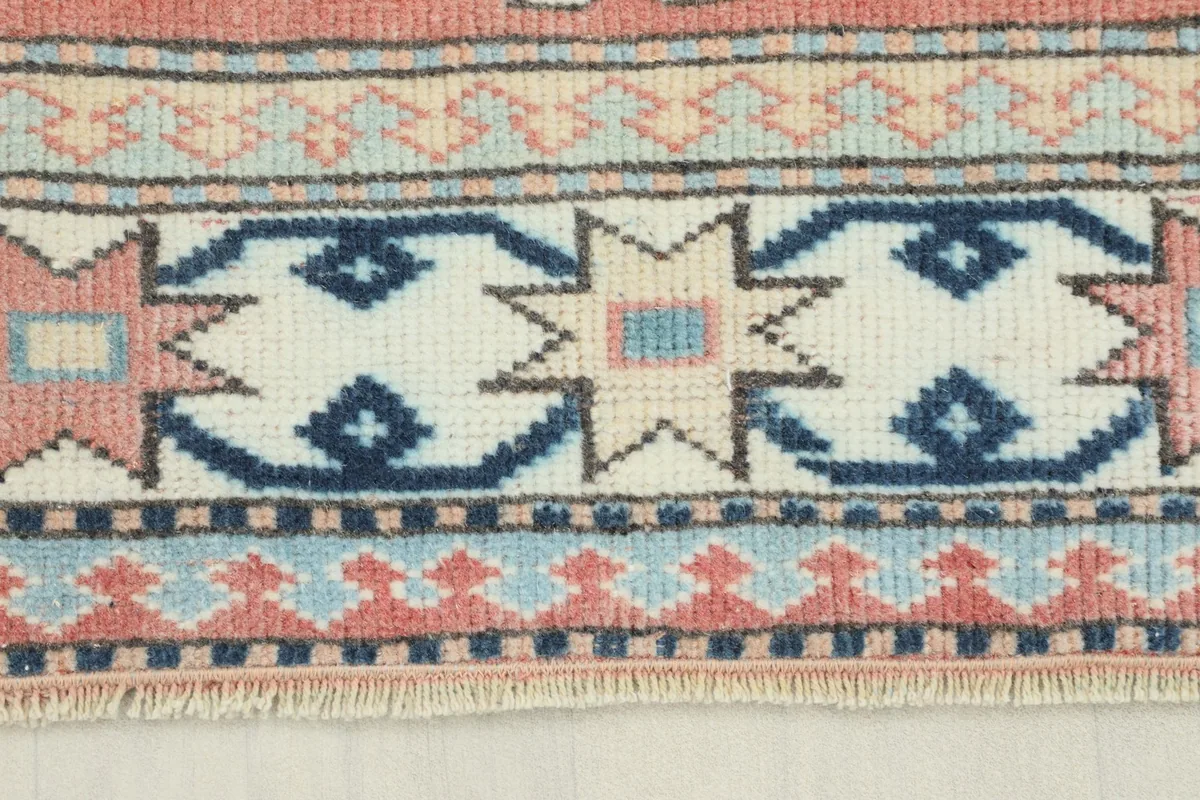 Close-up detail of the rug's border, featuring ivory, navy, and rose geometric star motifs and fringe.