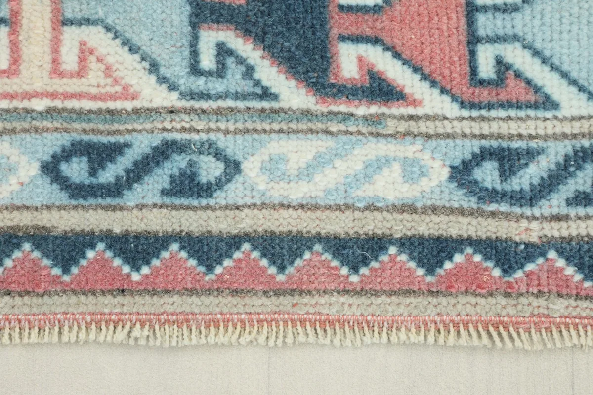 Close-up of the rug's border showing a light blue and rose geometric pattern and fringe.