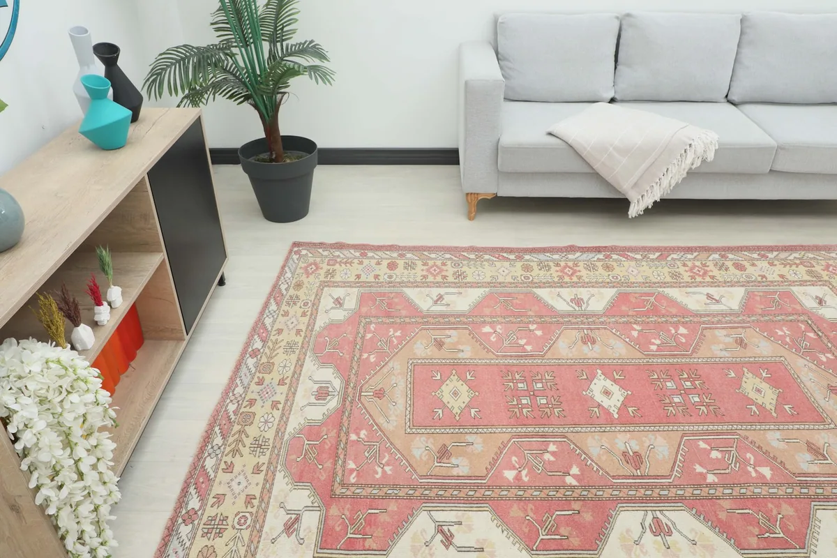Angle view of the rose and beige vintage rug in a living room, showing its placement relative to a sofa.