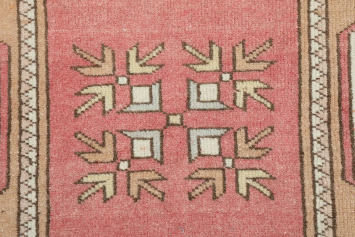 Close-up of a central geometric motif in rose, beige, and ivory, showcasing the hand-knotted detail.