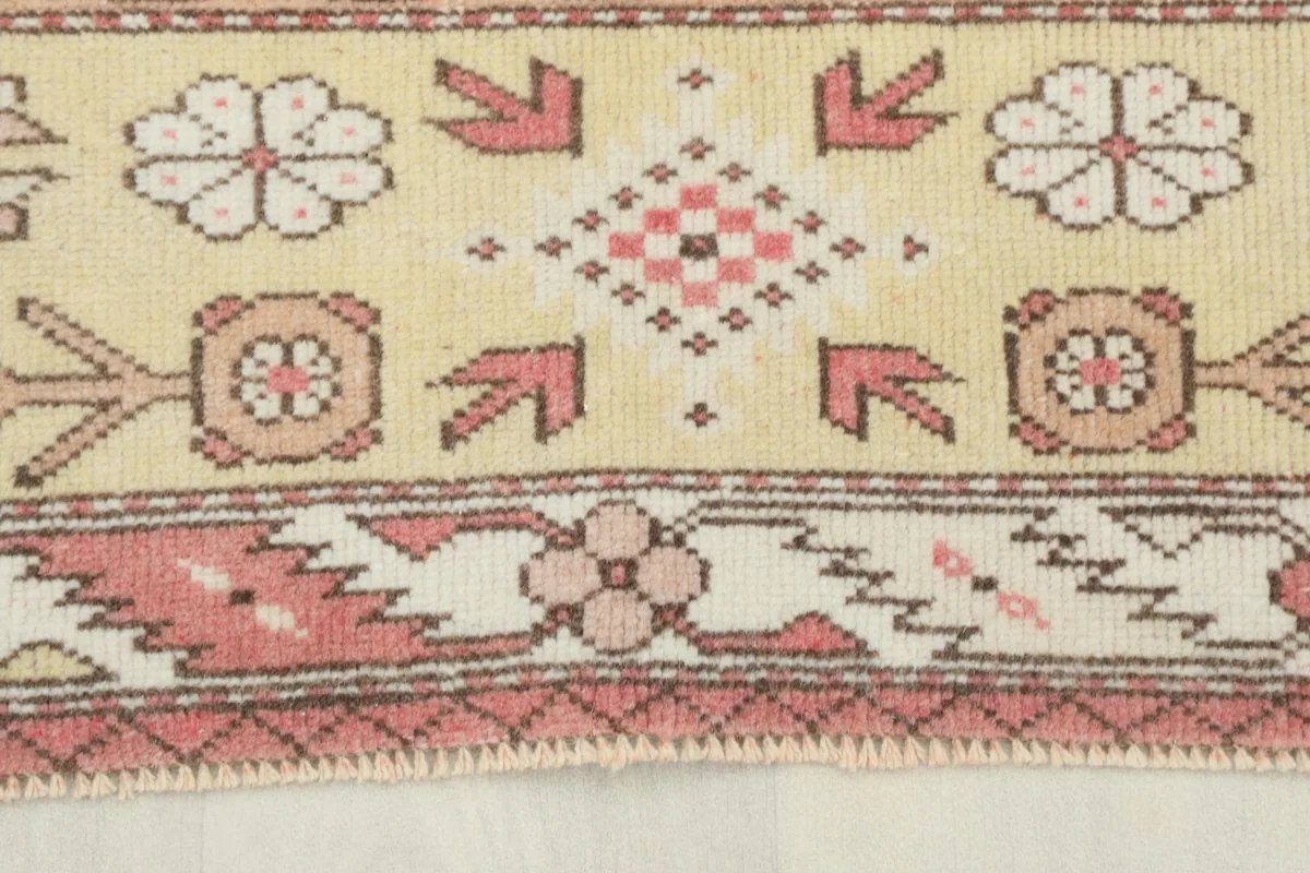 Close-up detail of the beige border with rose and ivory tribal floral motifs on the vintage rug.