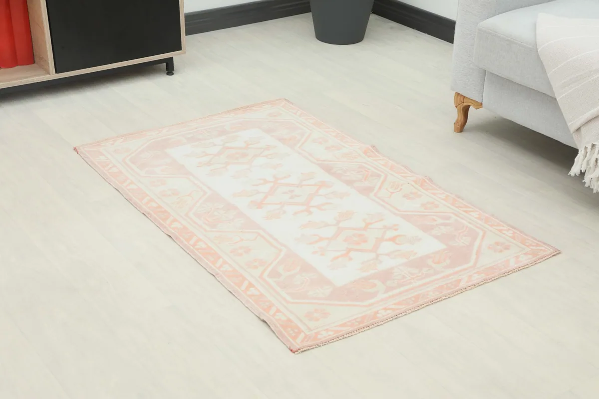 Angle view of the rose and ivory vintage area rug on a light floor, showing its placement in a room.