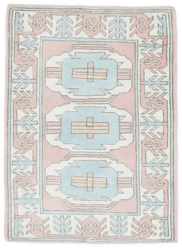 Full overhead view of the vintage pink and blue geometric Anatolian rug on a white background.
