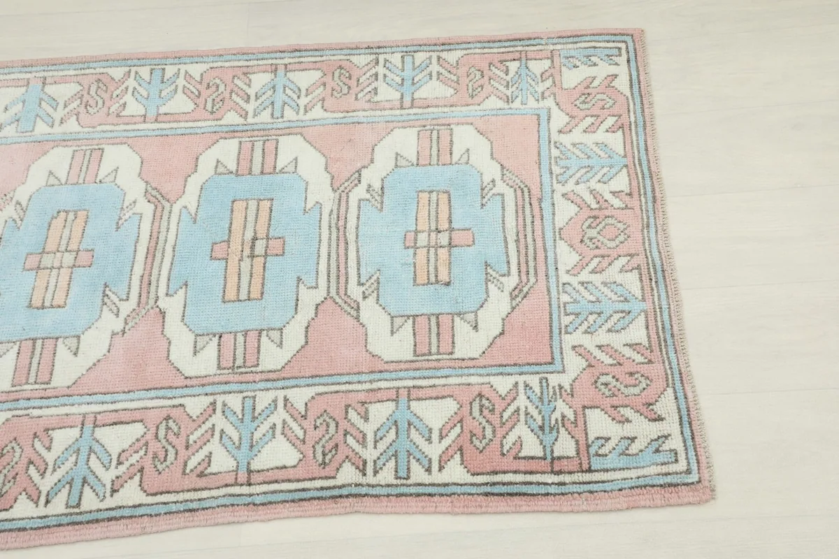 Close-up view of the upper right corner of the rug, highlighting the pink, blue, and beige geometric border.