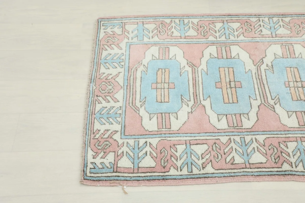 Close-up view of the lower left corner of the rug, showing the tribal patterns and soft colors.