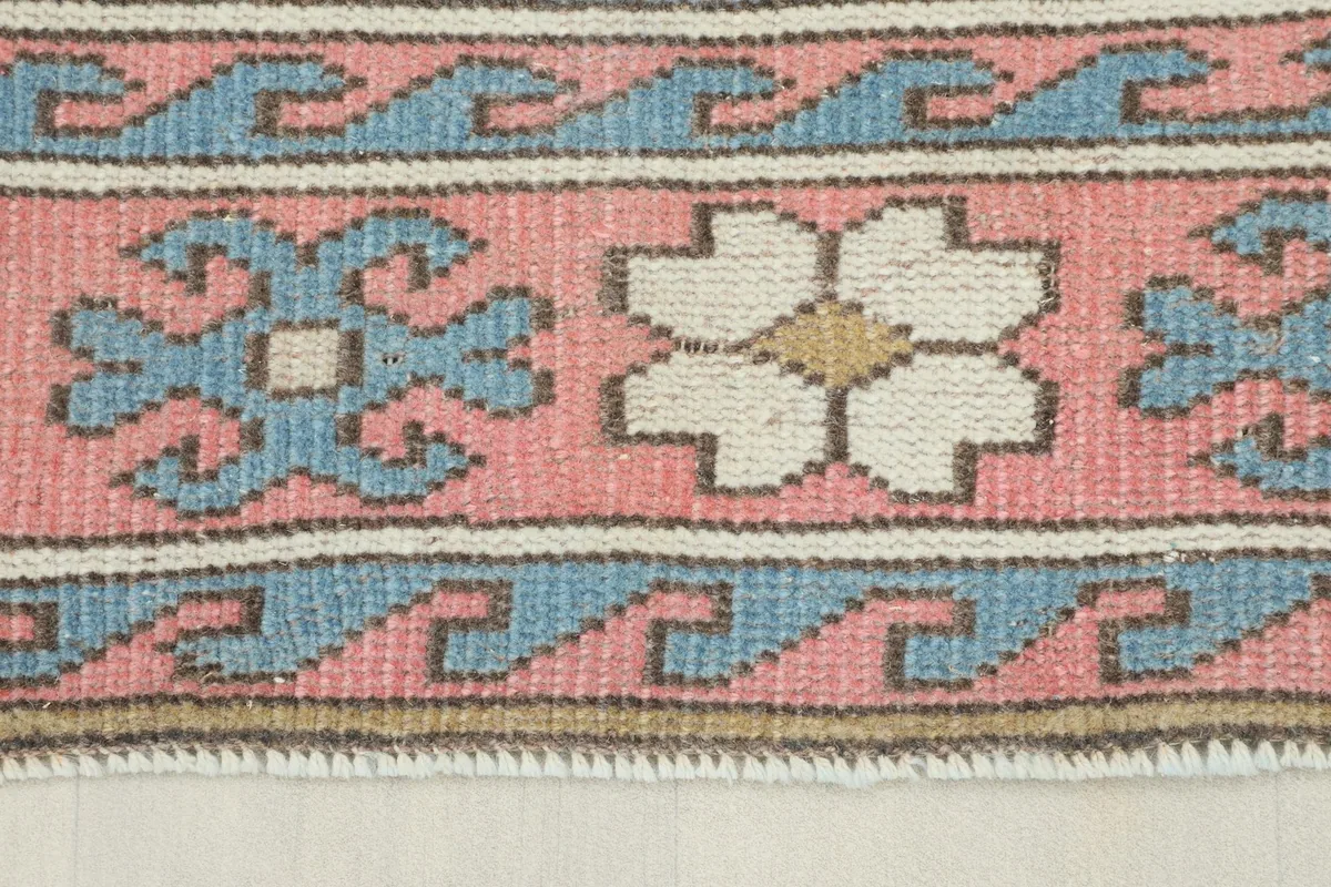 Close-up detail of the pink border with blue and ivory geometric motifs and fringe.