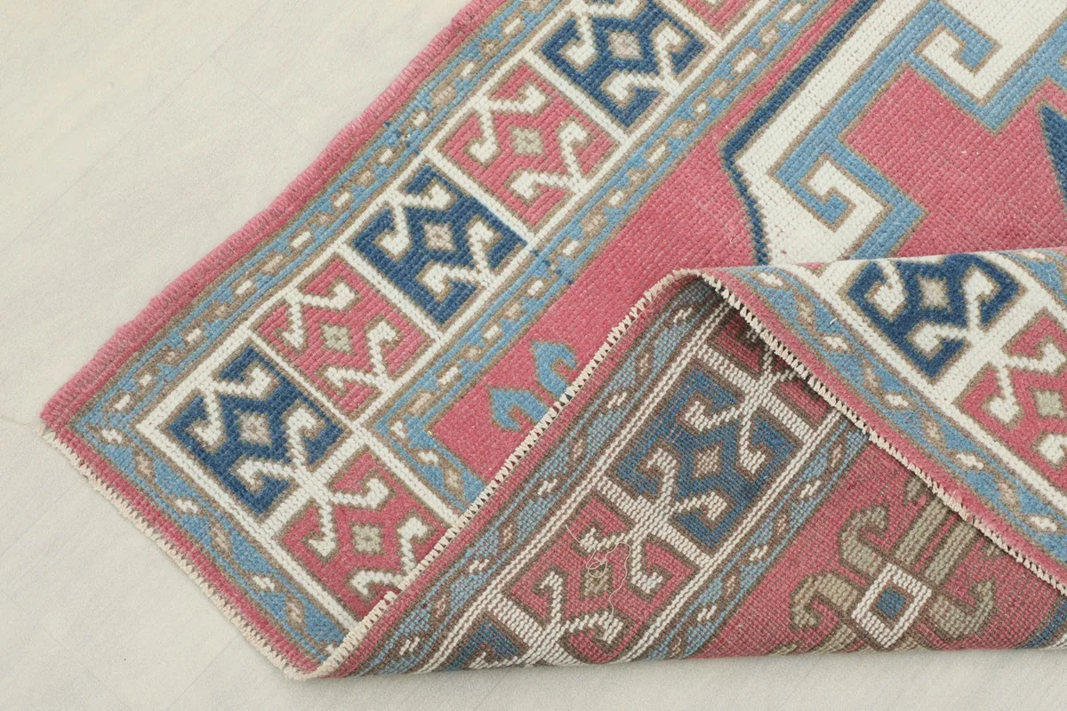 Folded corner of the rug revealing the thickness and intricate border designs in blue, gray, and rust
