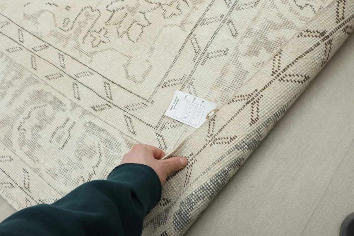Hand touching the rug's low wool pile, revealing its vintage texture and construction