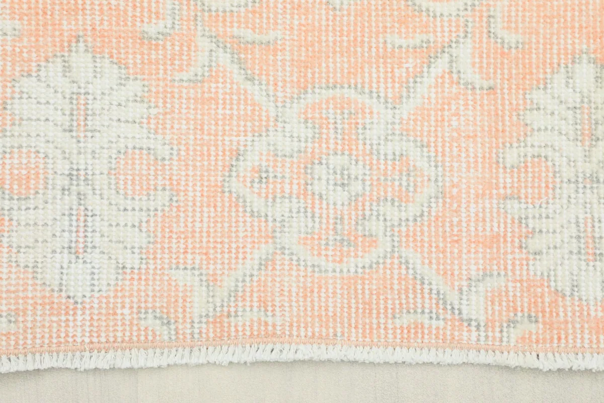 Close-up view of the rug's short fringe and faded rose and ivory geometric pattern