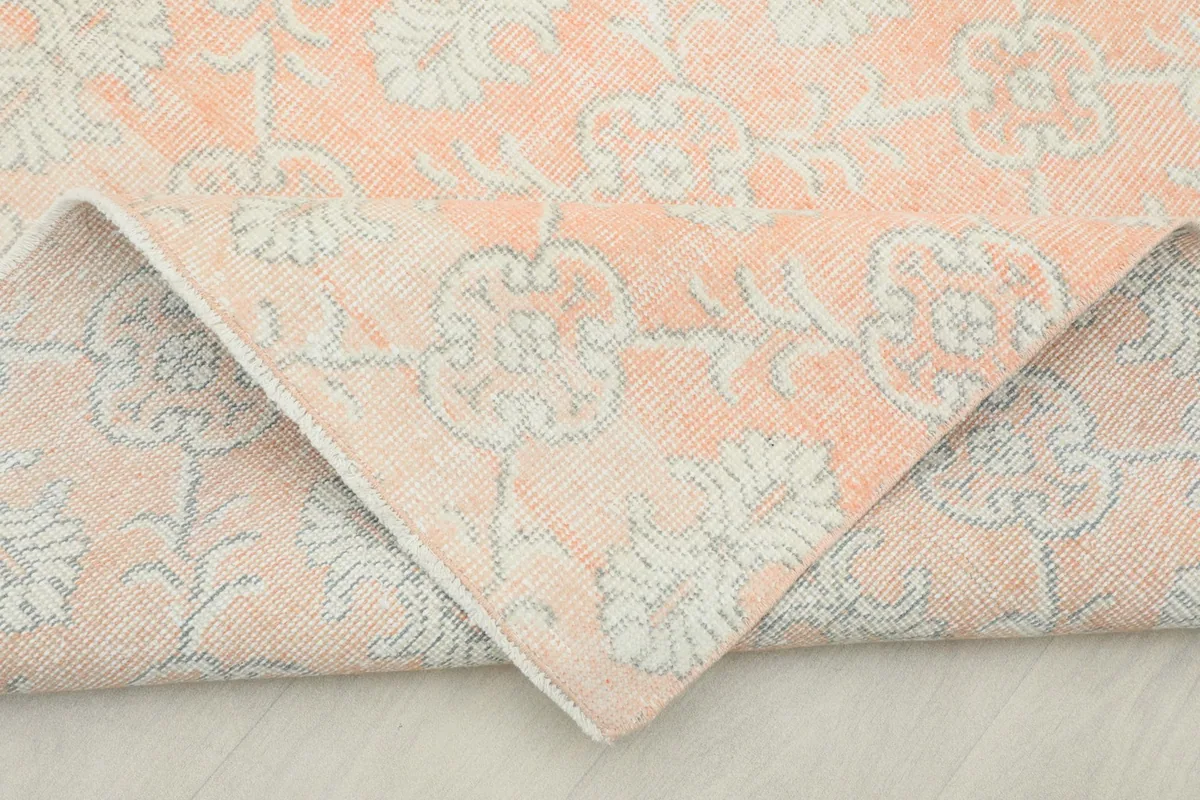 Corner of the rose rug folded back, revealing the hand-knotted wool pile and cotton foundation