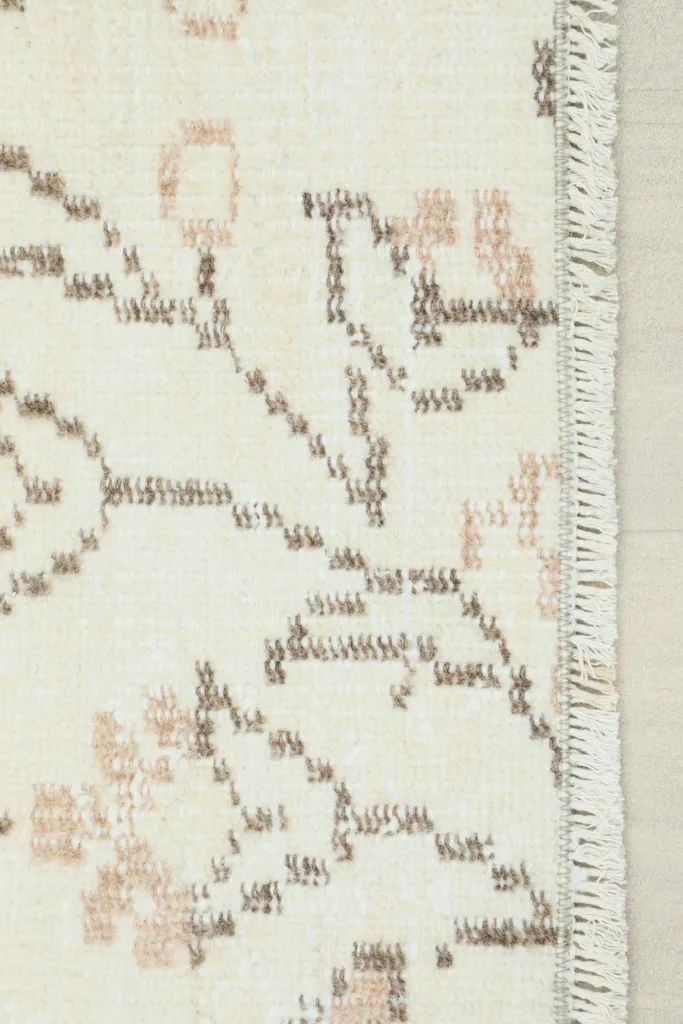 Close-up detail of the rug's edge, showing the cream field, tan geometric patterns, and short fringe.