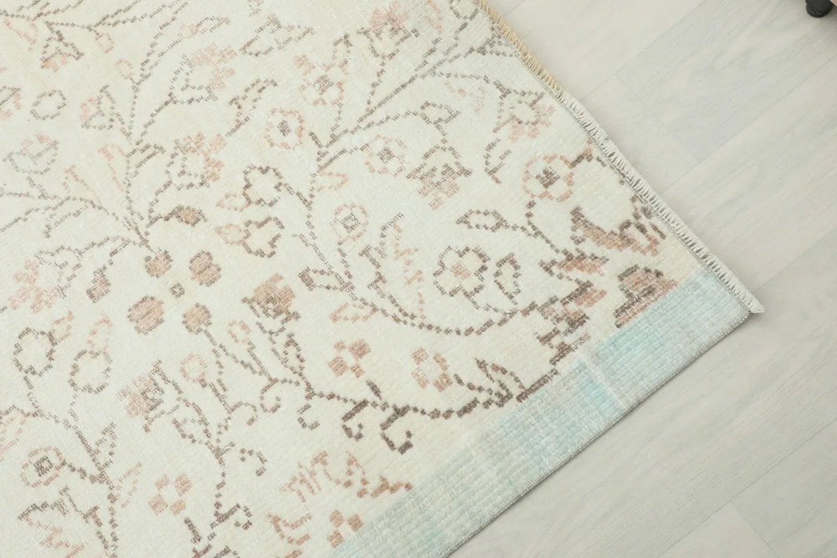 Corner view of the rug, detailing the subtle light blue border and the transition to the main cream field.