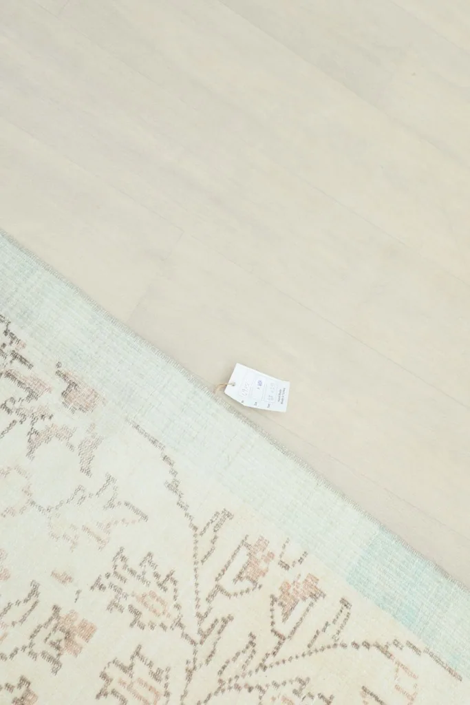 Partial view of the rug's reverse side, showing the hand-knotted cotton foundation and the light blue border.