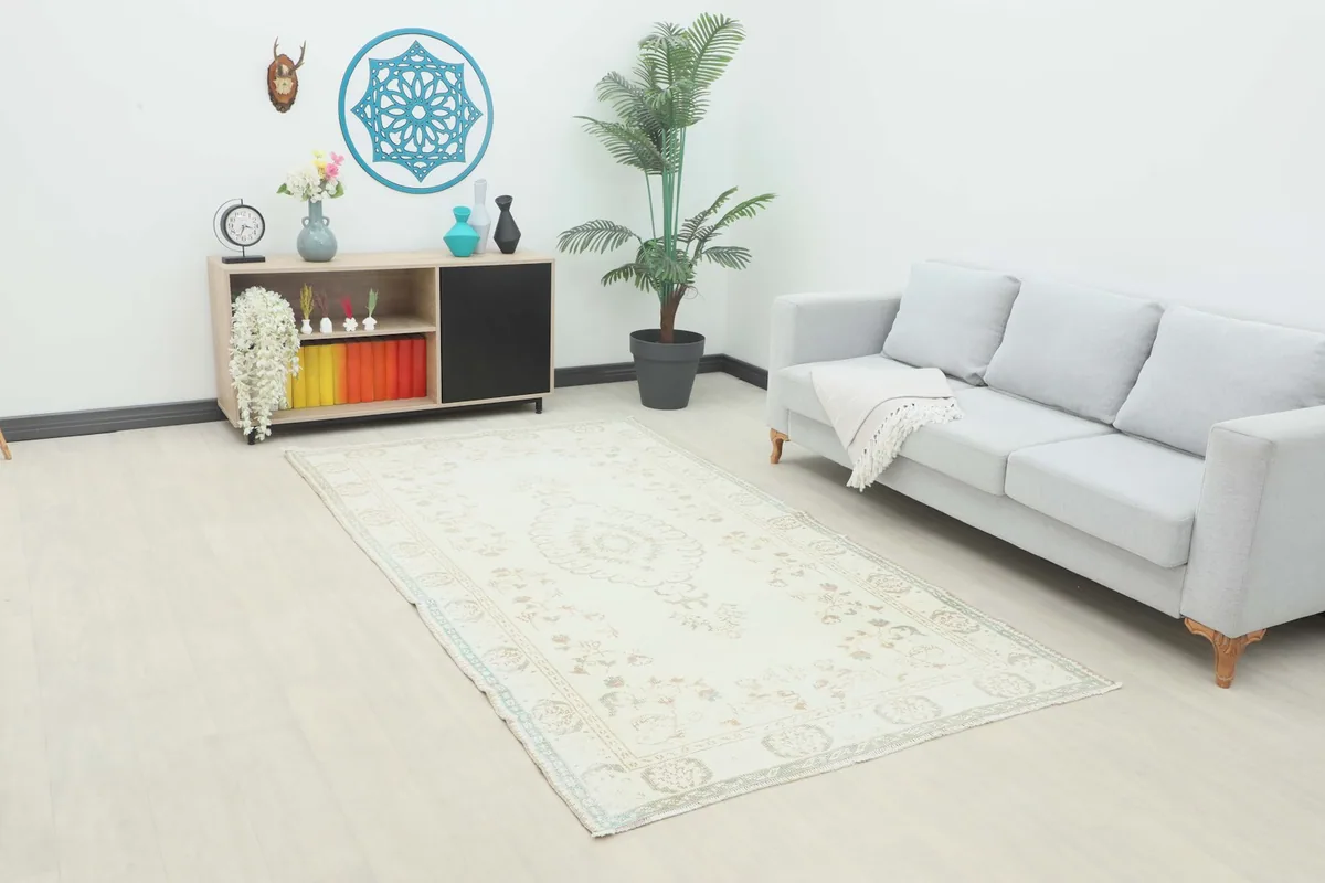 Ivory vintage rug displayed in a room setting with a light gray sofa and a plant, showing its full length.
