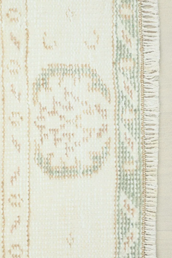 Close-up detail of the rug's border and a faded medallion motif in olive and beige tones.