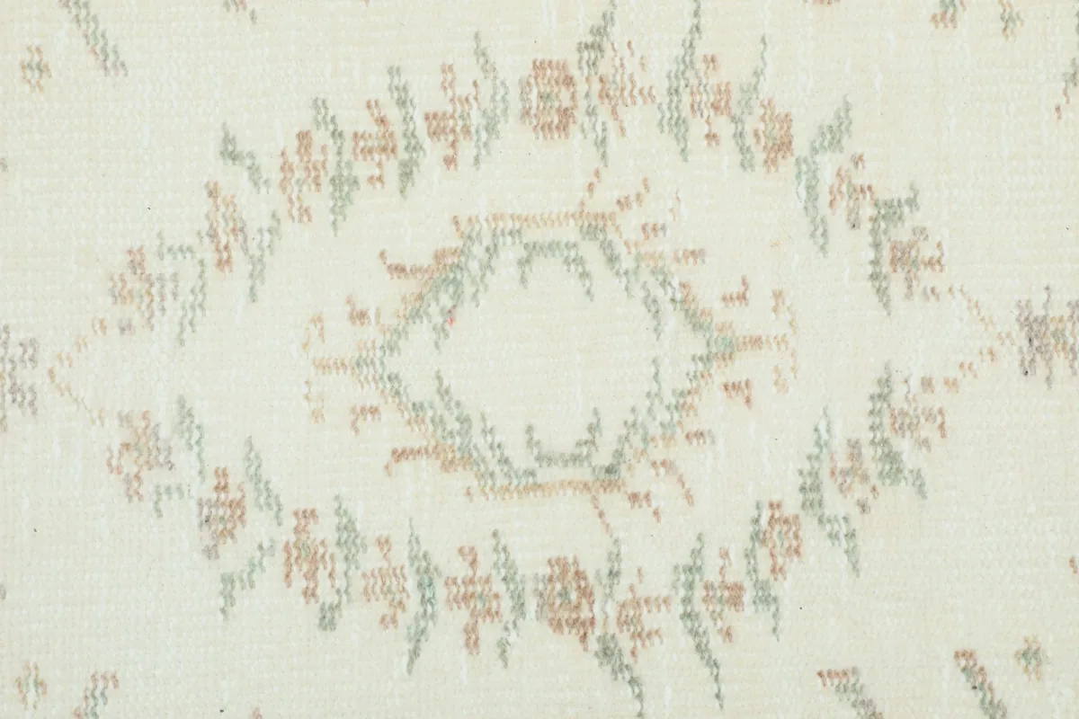 Close-up of a faded floral motif on the rug's ivory field, showing wear and color variations.