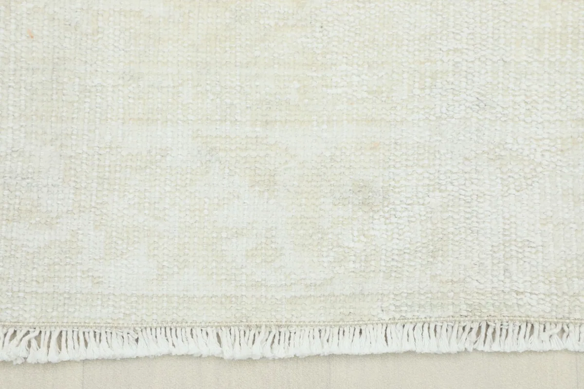 Close-up detail of the rug's texture and subtle, faded ivory and gray patterns with short fringe.