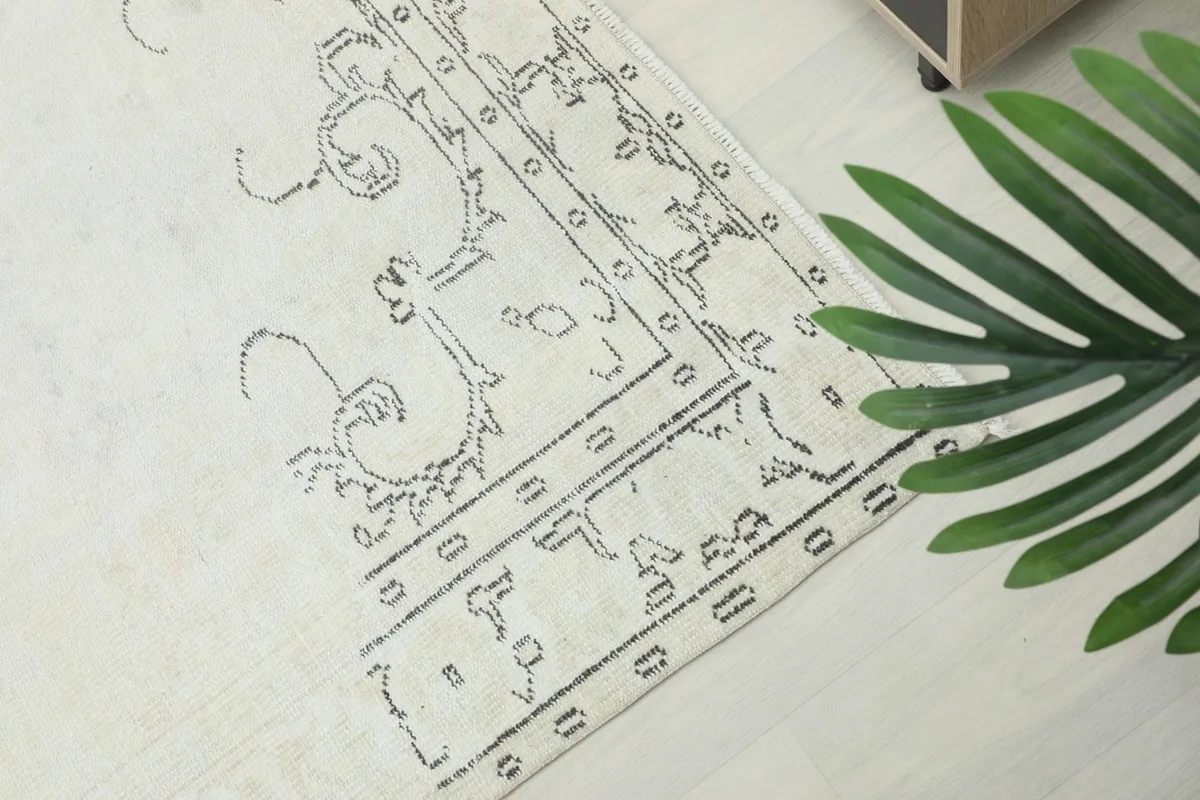 Detailed close-up of the rug's border, featuring faded gray scroll-like motifs on an ivory field.