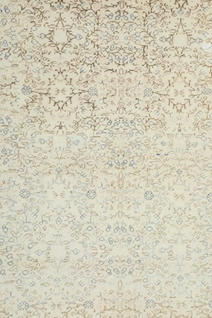 Close-up view of the subtle floral and vine patterns in beige, brown, and light blue on the rug