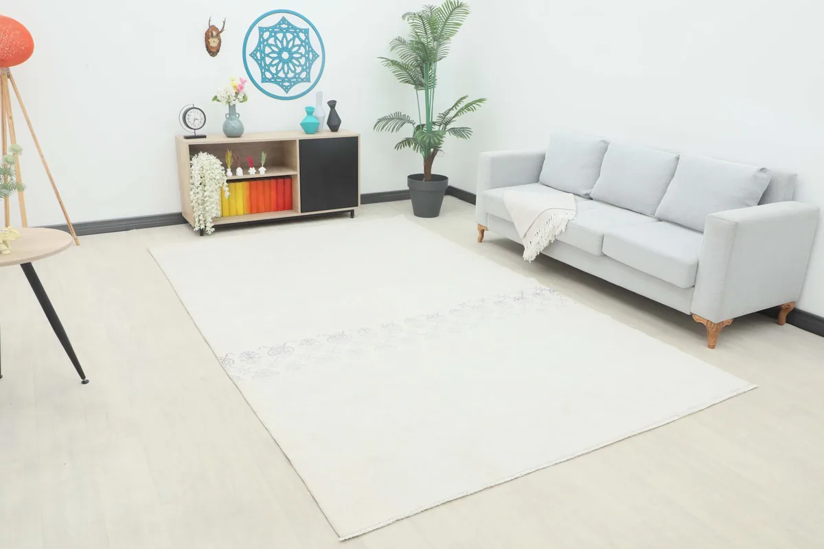 Ivory vintage rug displayed in a bright room with a gray sofa and wooden furniture, showing its scale.