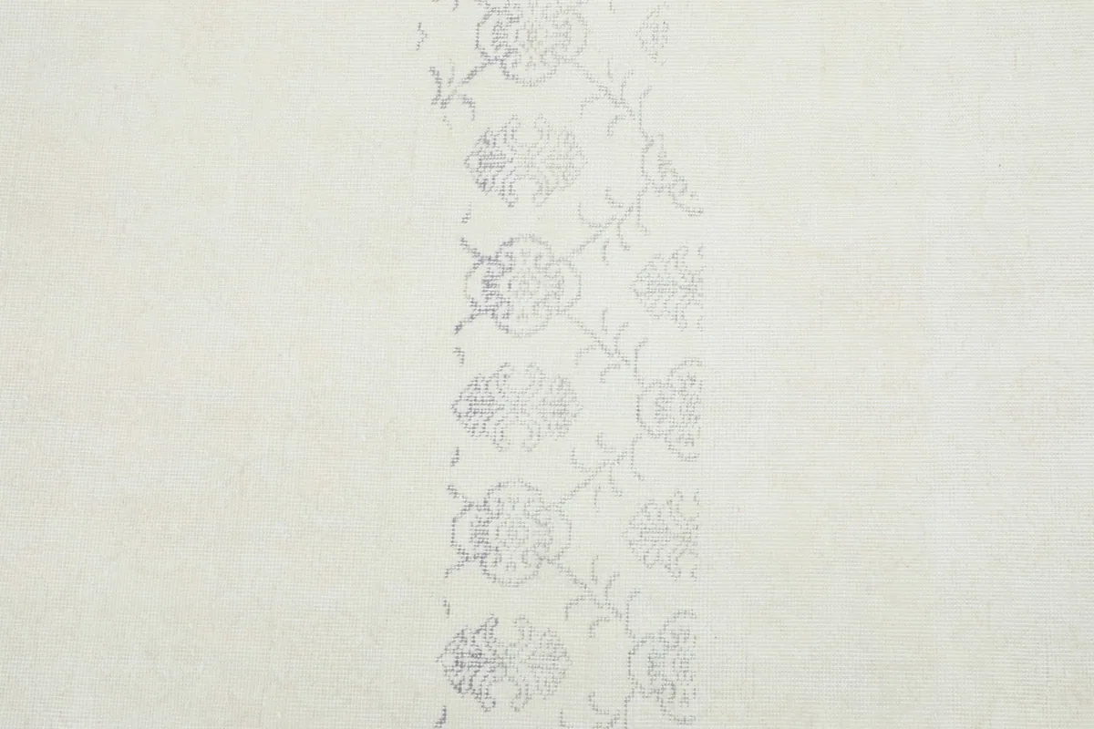 Detailed view of the subtle, faded floral and geometric patterns visible in the ivory rug's field.