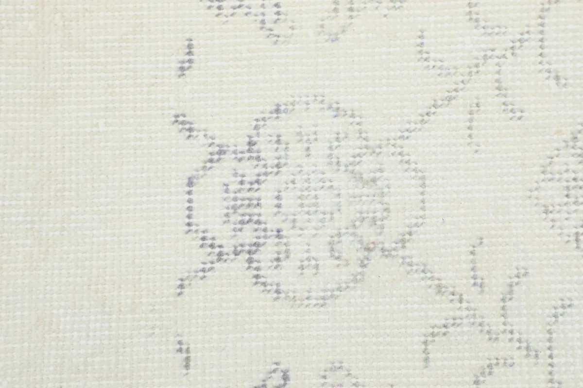 Close-up of a single faded floral motif within the ivory rug, highlighting the intricate hand-knotting.