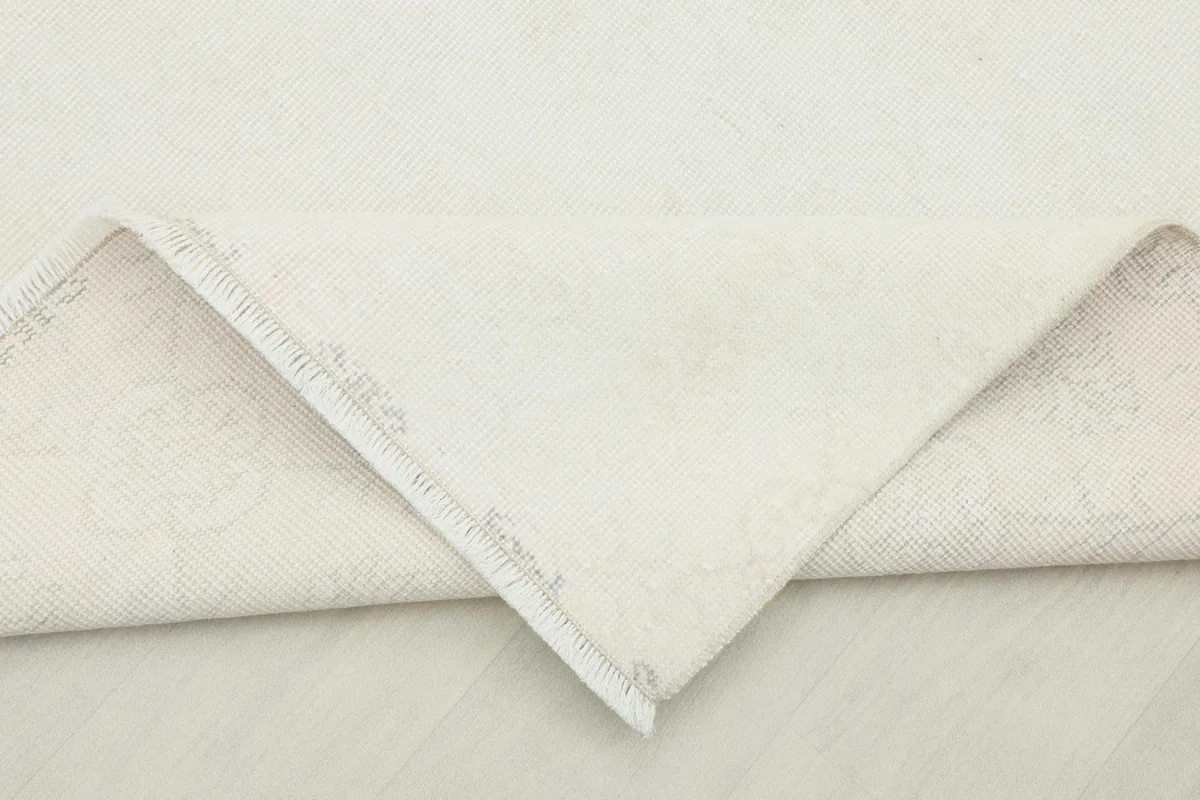 Corner of the ivory rug folded back to show the reverse side, revealing the cotton foundation and knotting.