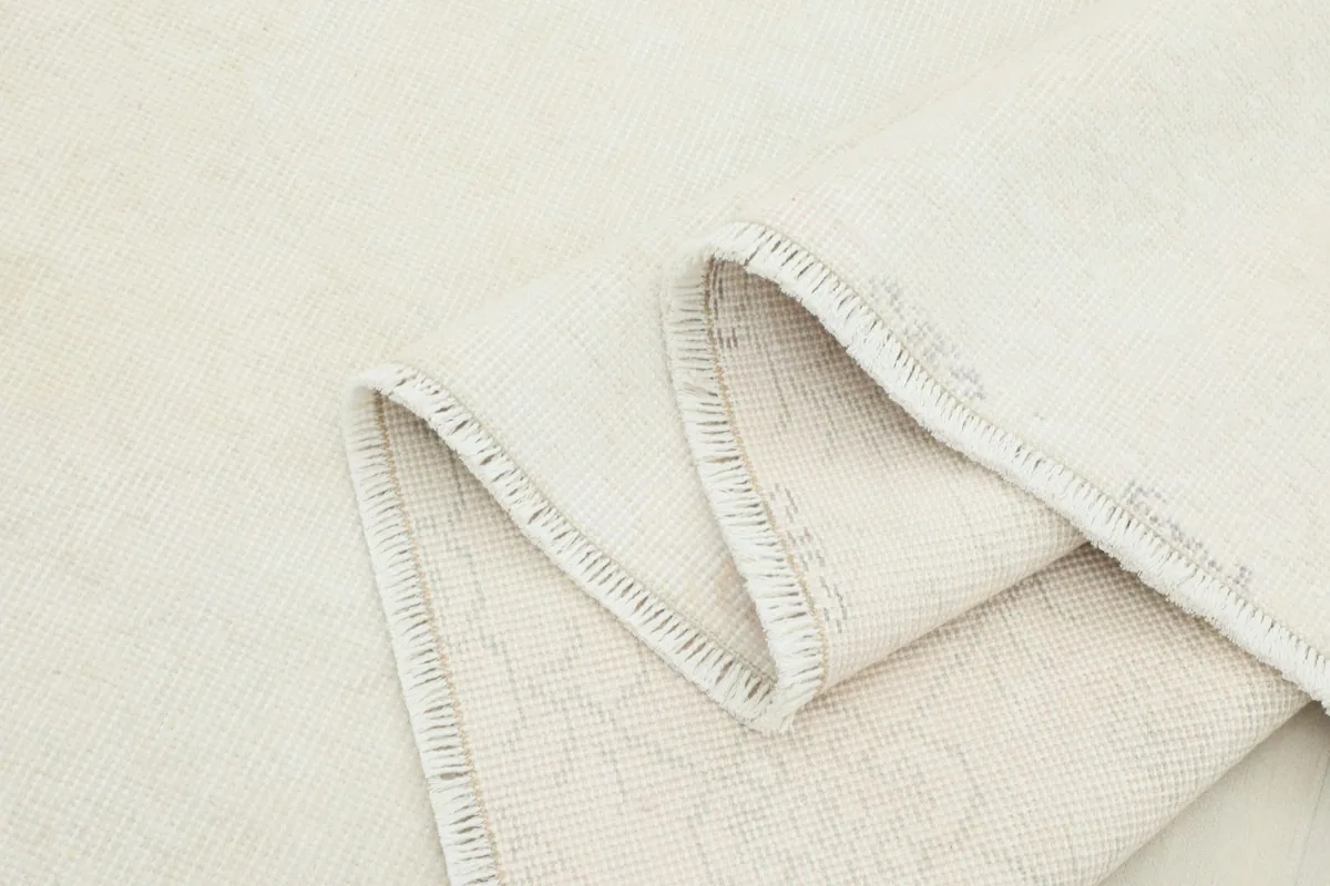 Folded edge of the ivory rug, showing the fringe and the density of the hand-knotted wool pile.