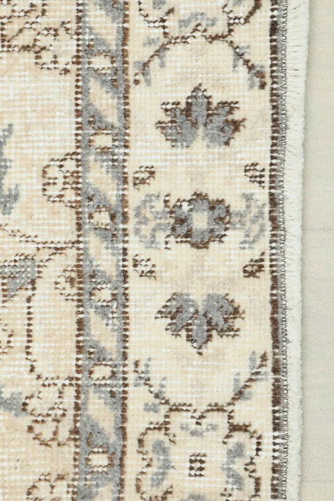 Close-up view of the rug's border showing the intricate gray and beige floral patterns and fringe.
