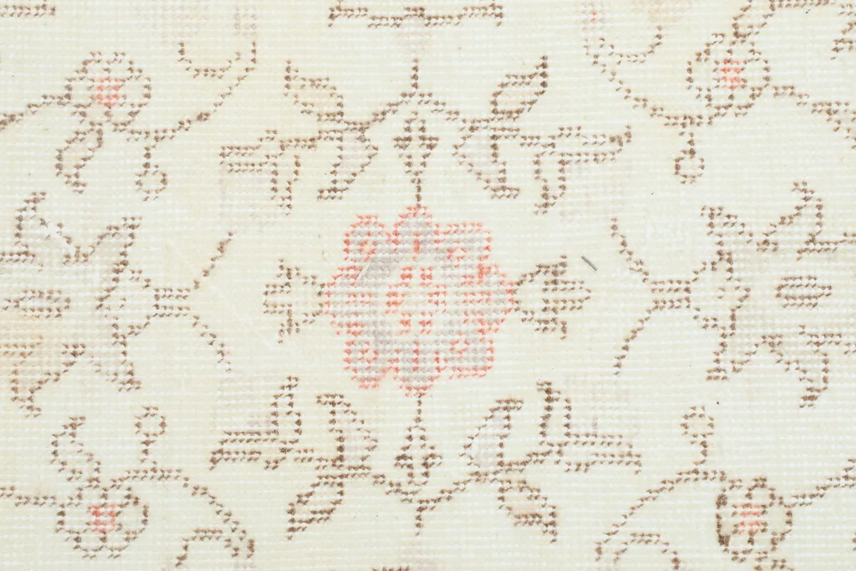 Close-up showing a central rose-colored floral element with surrounding tan patterns on the ivory pile.