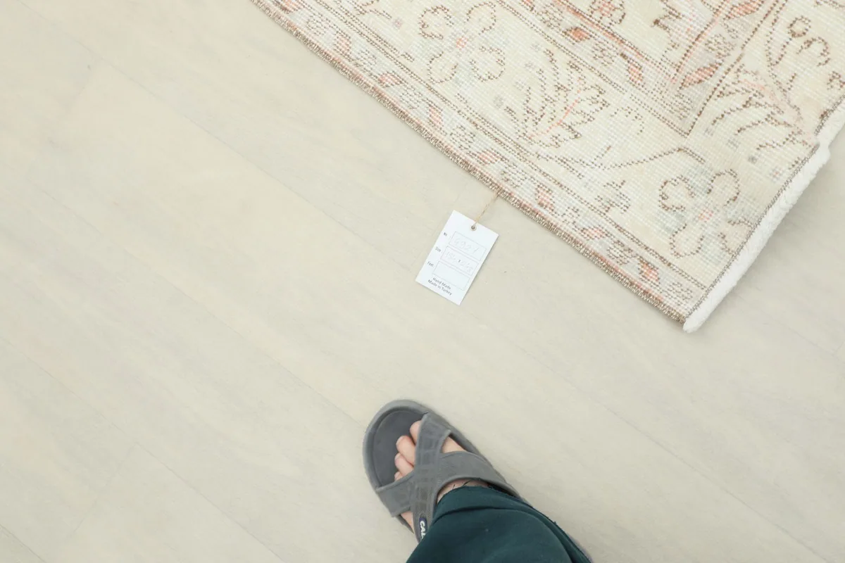 Overhead view of a corner of the rug with a tag, next to a person's foot, for scale.