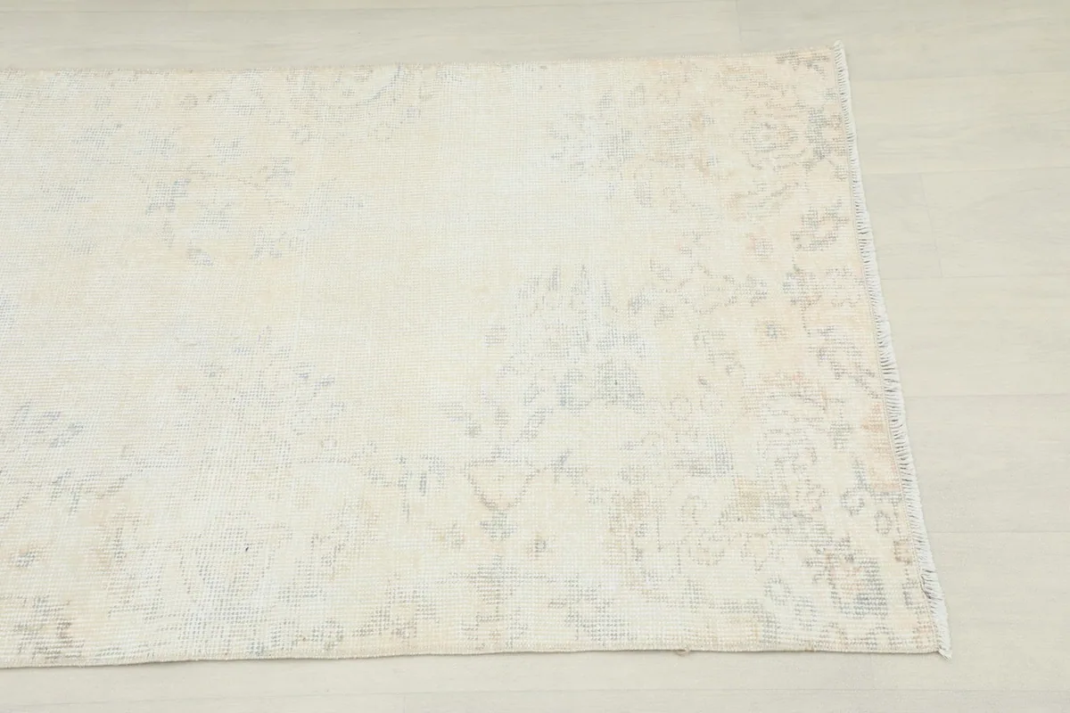 Close-up of one end of the cream runner rug, showing the subtle faded patterns.