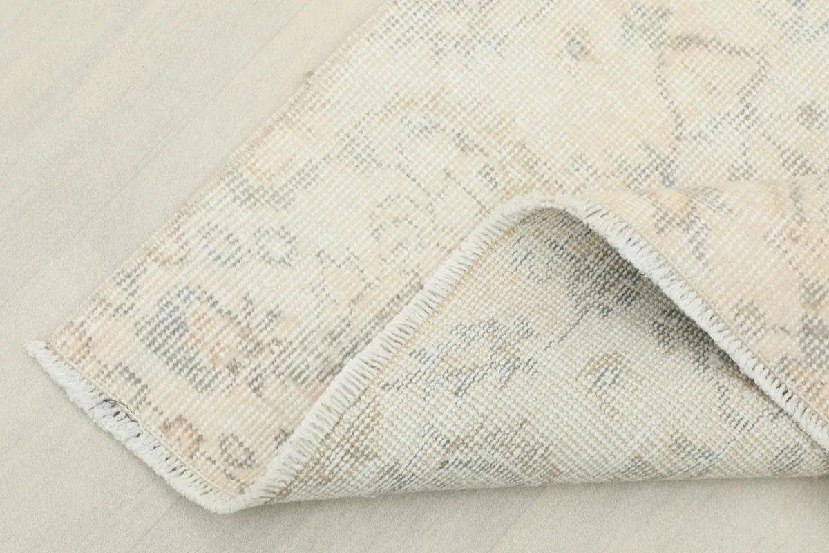 Corner of the rug folded back, showing the back of the hand-knotted cotton foundation.