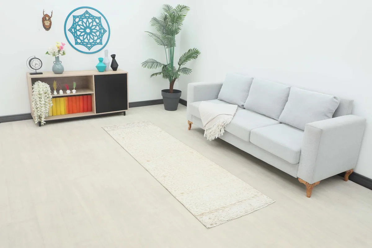 Cream runner rug placed in a modern living room setting next to a light gray sofa.