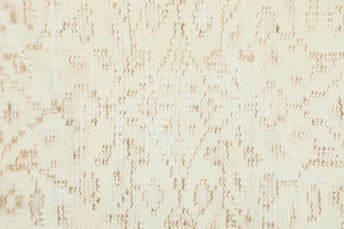 Macro view of the low pile and intricate hand-knotted details of the cream wool rug.