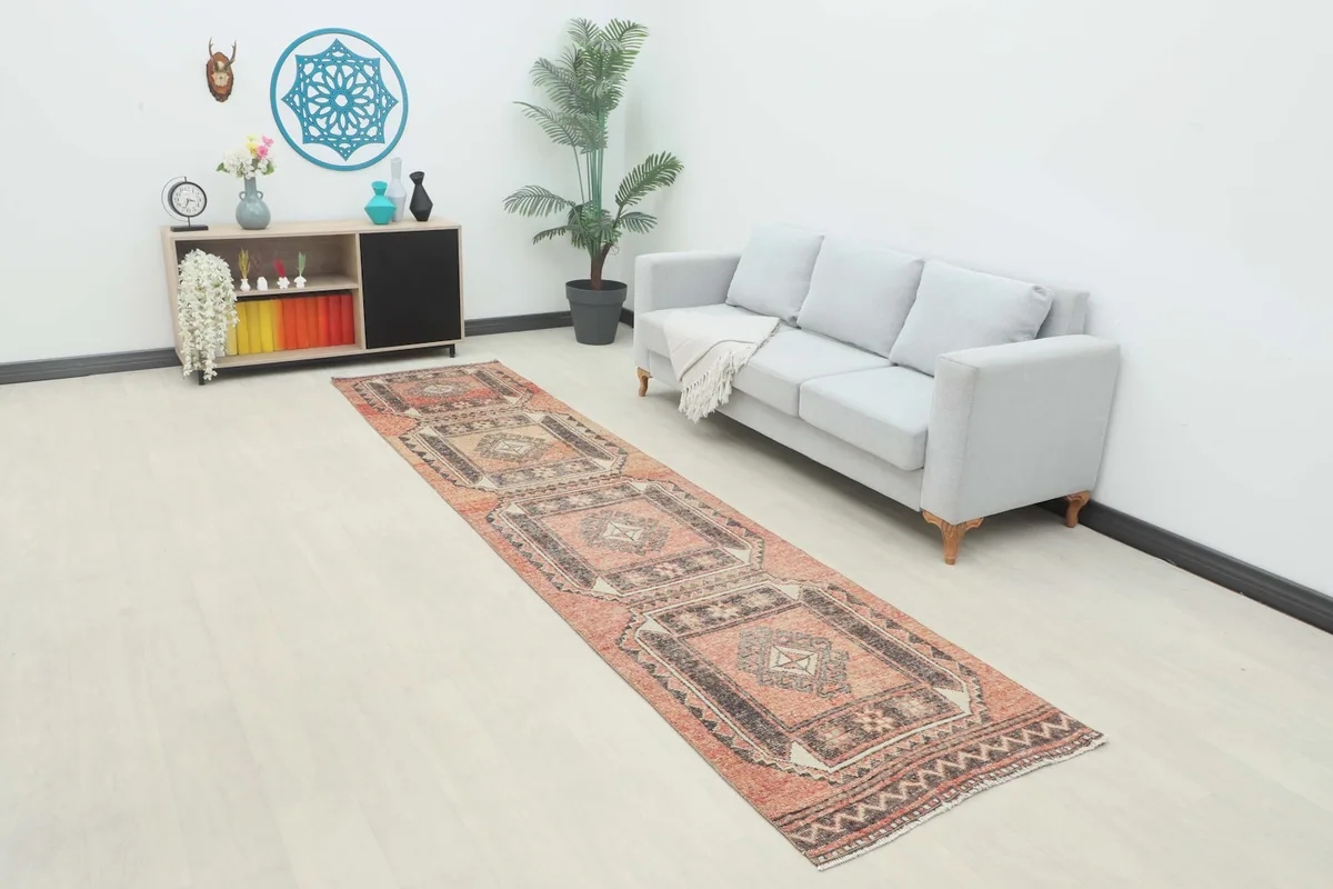 Vintage rust runner displayed in a modern room setting next to a gray sofa and dark cabinet.